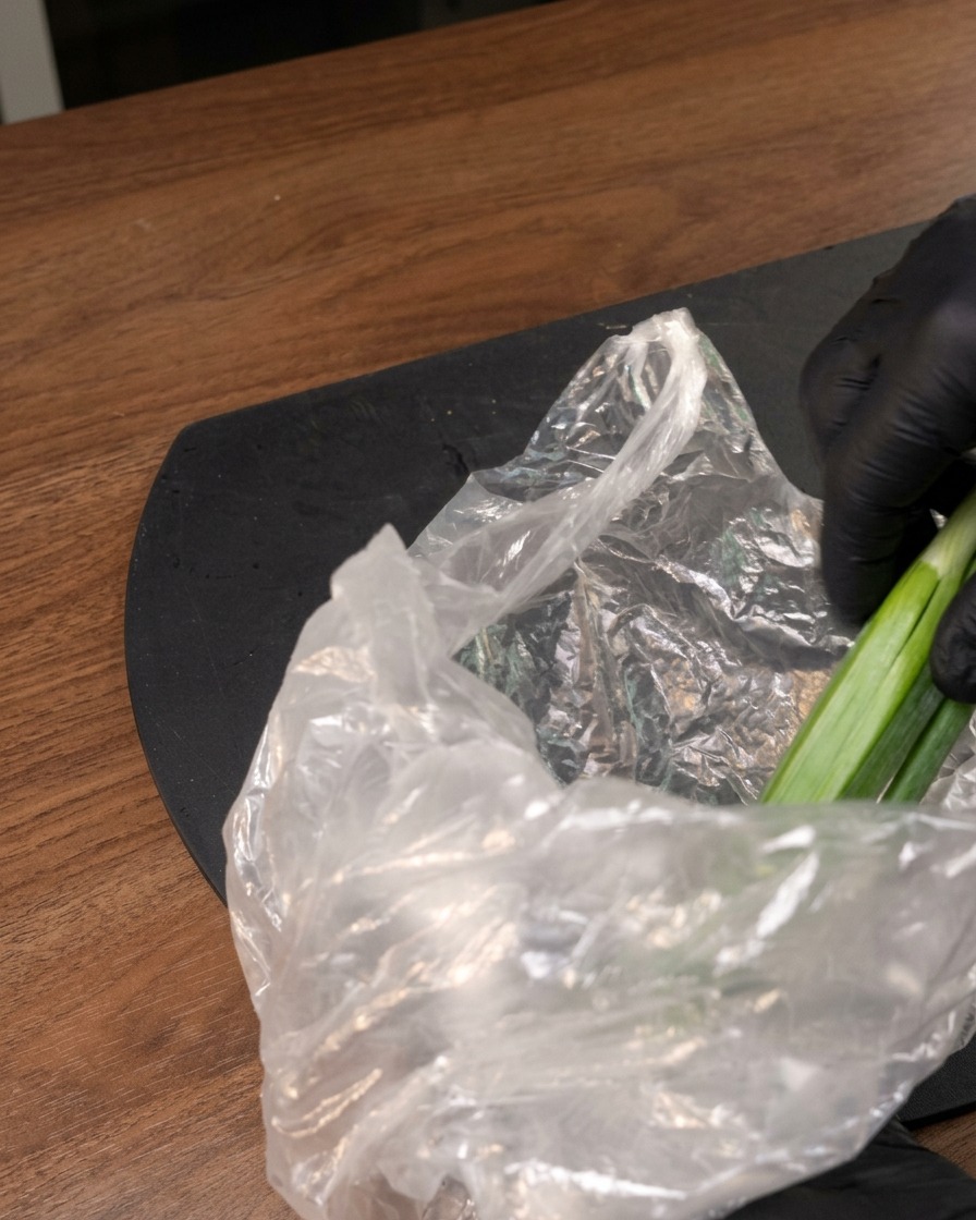 A gloved hand removing fresh green produce from a clear plastic bag on a dark surface.