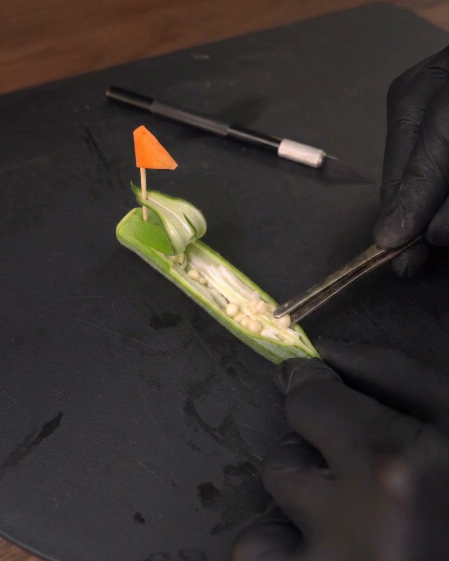 Using metal tweezers to carefully remove the seeds from the inside of the okra.