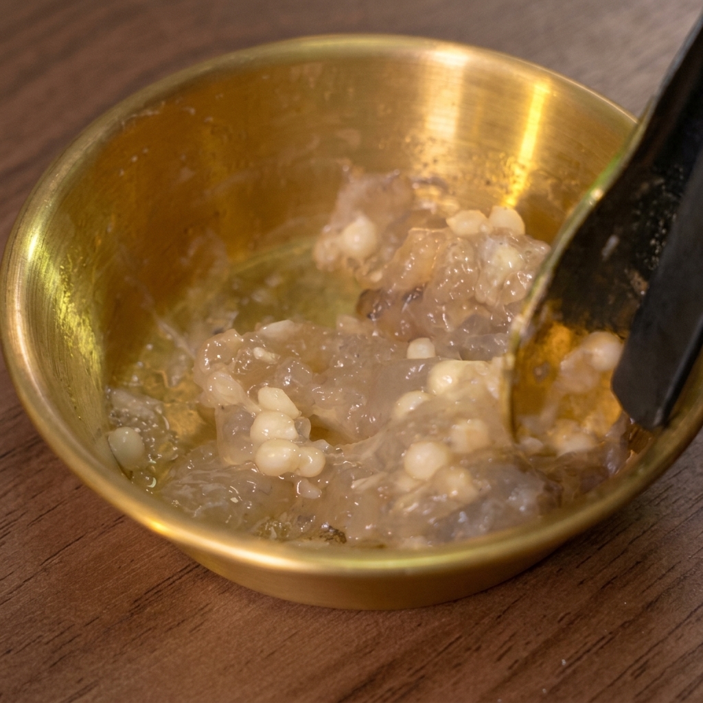 A spoon stirring minced shrimp and okra seeds in a golden bowl.