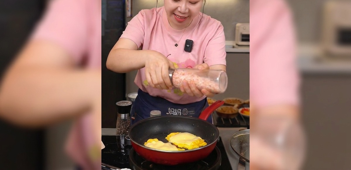 Hands holding a grinder and dispensing pink sea salt over a pan of cooked eggs and melted cheese.
