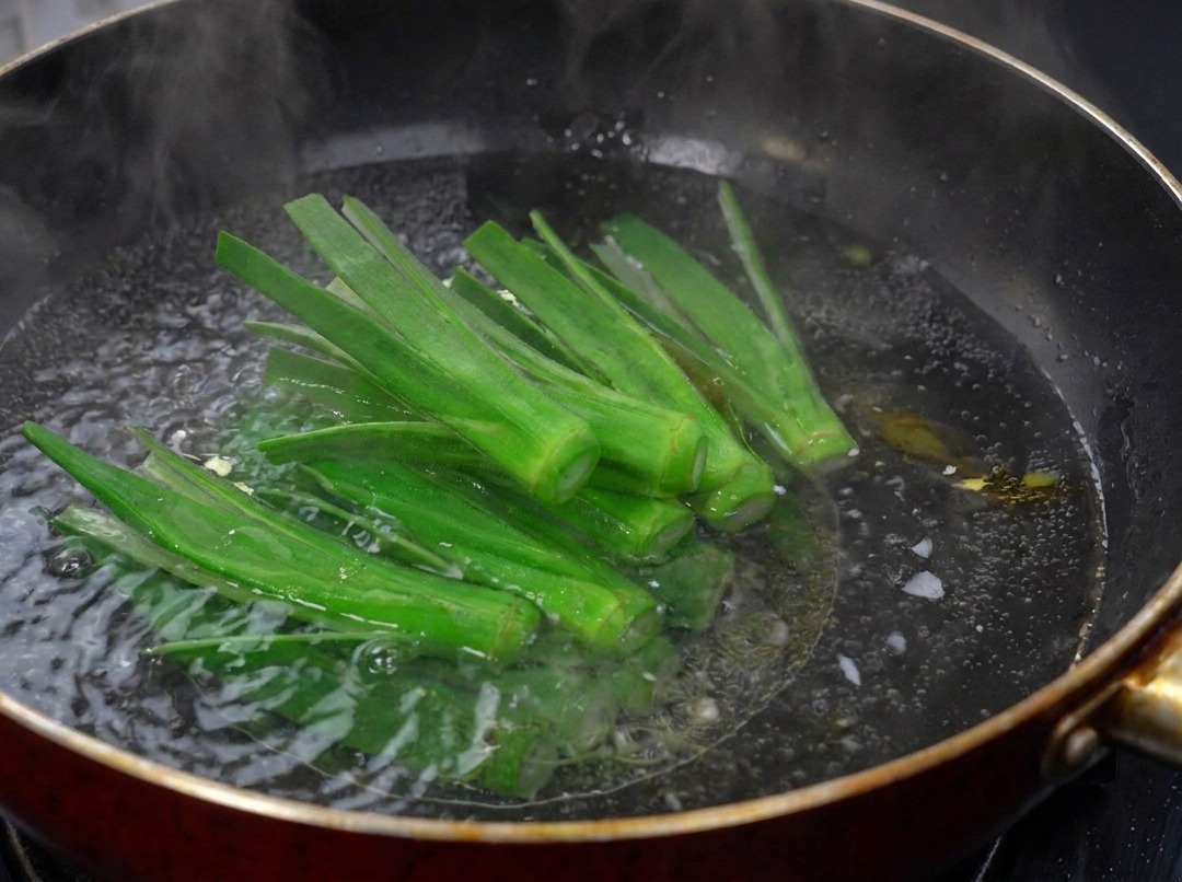 Freshly scored green okra strips blanching in a dark wok filled with bubbling boiling water.