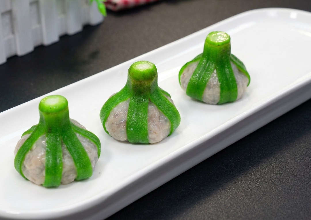 Three perfectly formed okra-wrapped shrimp balls arranged upside down on a long white rectangular plate, ready for the steamer.