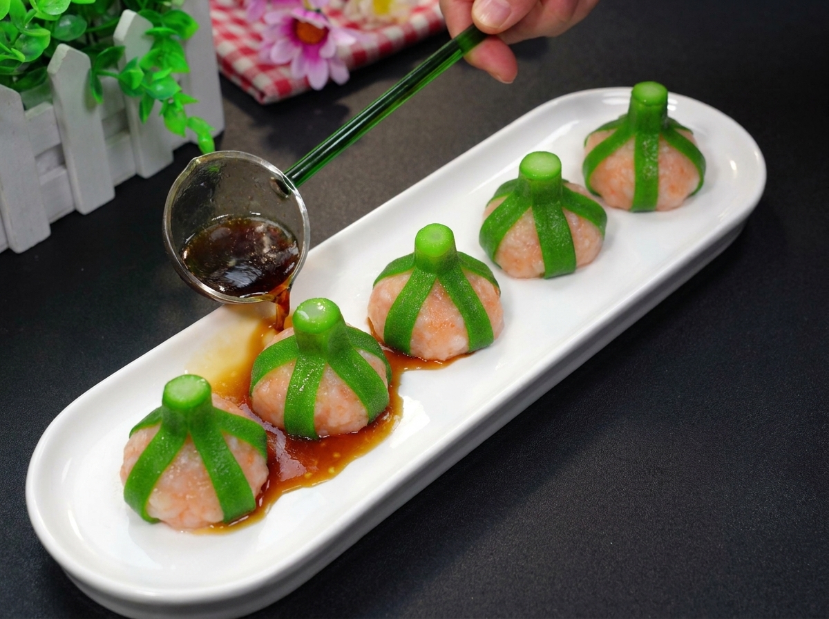 A hand using a small metal ladle to pour a dark, glossy sauce over steamed pink shrimp balls wrapped in green okra strips on a white serving plate.