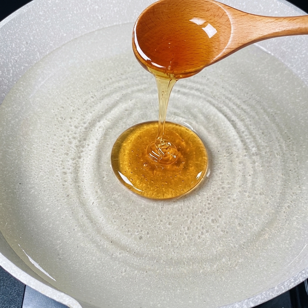 A wooden spoon pouring a steady stream of golden cooking oil into a pan of hot water.