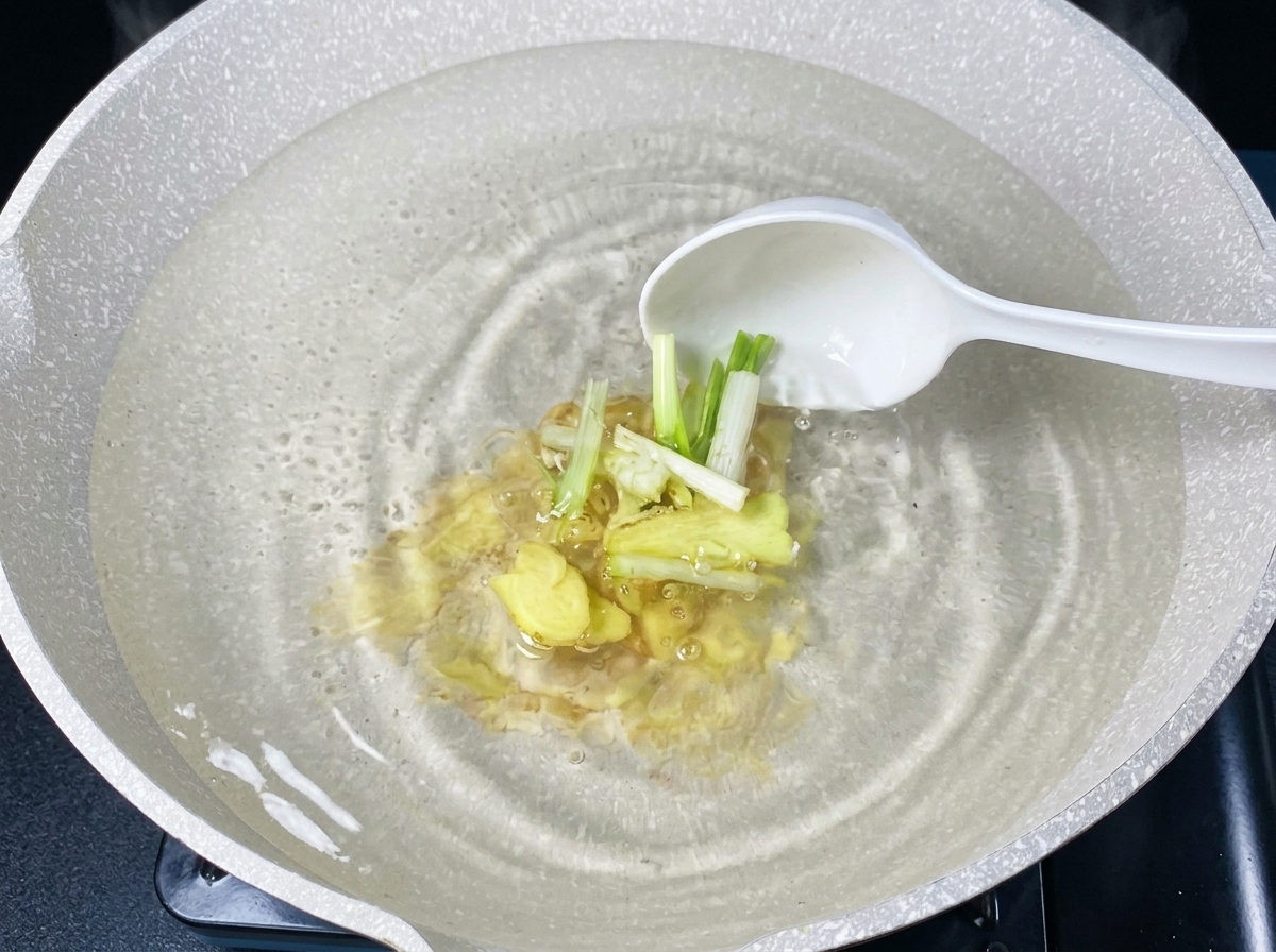 Fresh sliced ginger and scallion segments being added into boiling water with a white ladle.