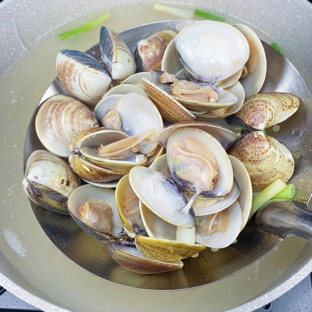 A metal slotted spoon holding hot, cooked clams with fully opened shells, freshly scooped from boiling water.