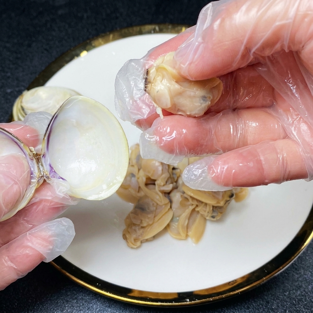 Gloved hands separating cooked clam meat from its shell over a plate holding more clam meat.