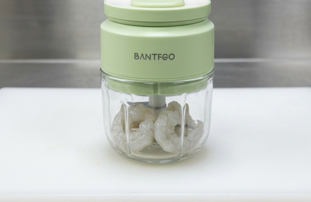 Raw peeled shrimp placed inside a small green food processor, ready to be blended into a paste.