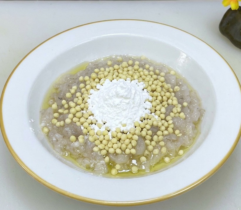 A white bowl containing raw shrimp paste topped with fresh okra seeds and cornstarch, ready to be mixed together.