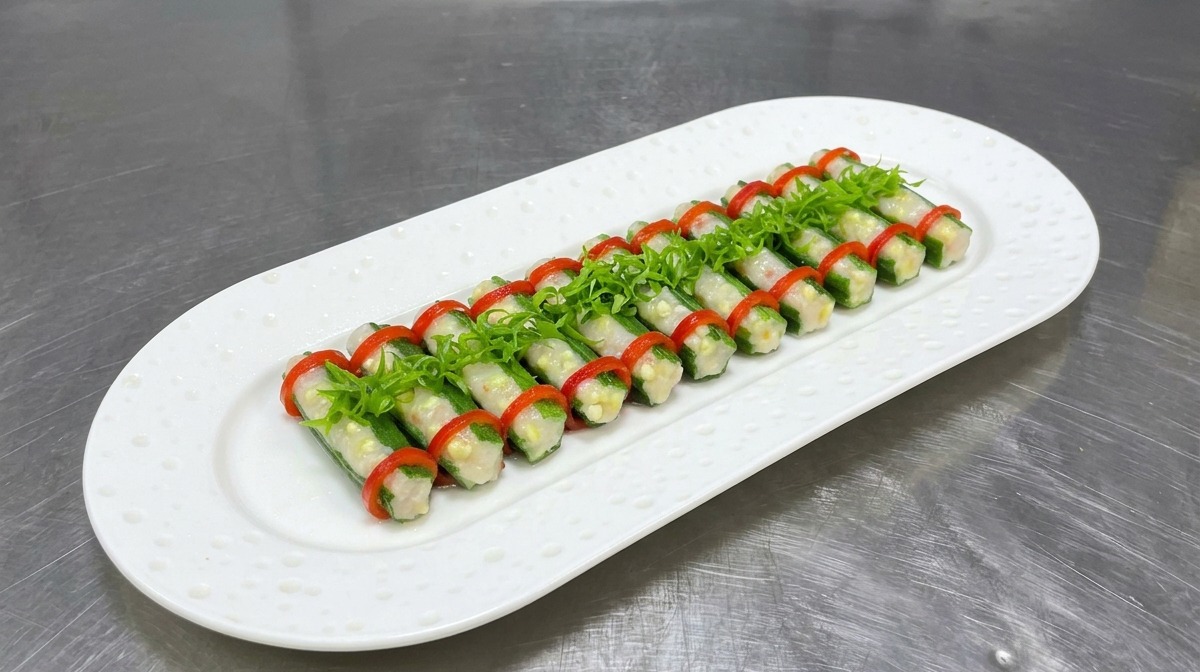 Steamed stuffed okra wrapped in red chili rings, arranged neatly on a white oval plate and topped with fresh curled scallions.