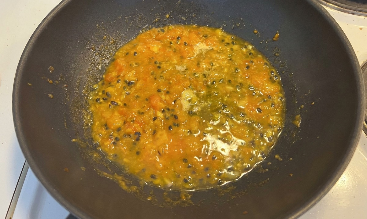 Seasoning powder sitting on top of a bubbling yellow and red tomato-passion fruit mixture.