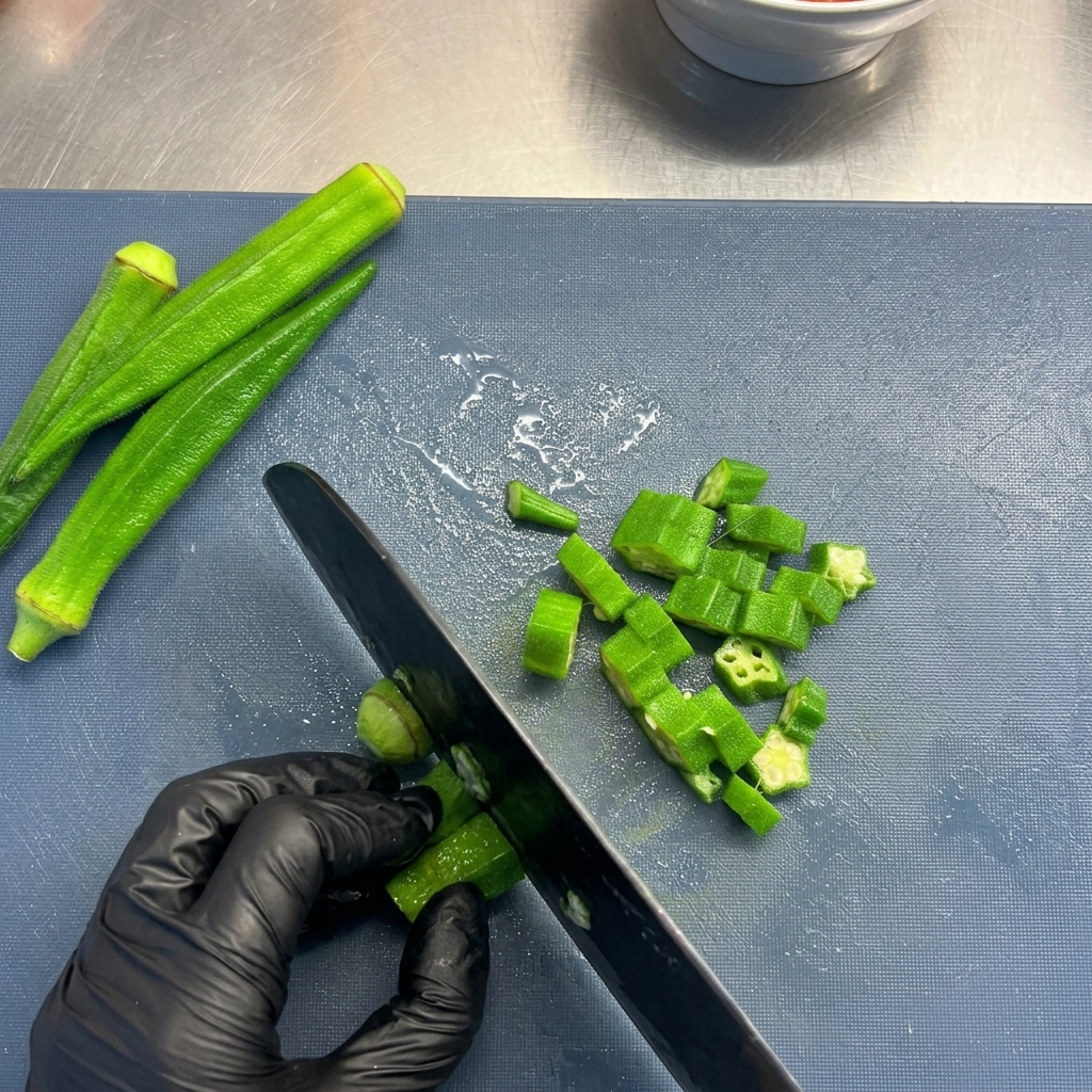 A person wearing black gloves slicing bright green okra into star shapes on a blue cutting board.