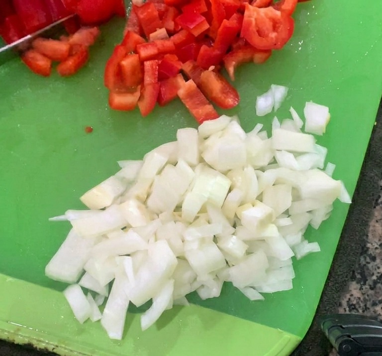 Diced white onions and chopped red bell peppers resting on a green cutting board.