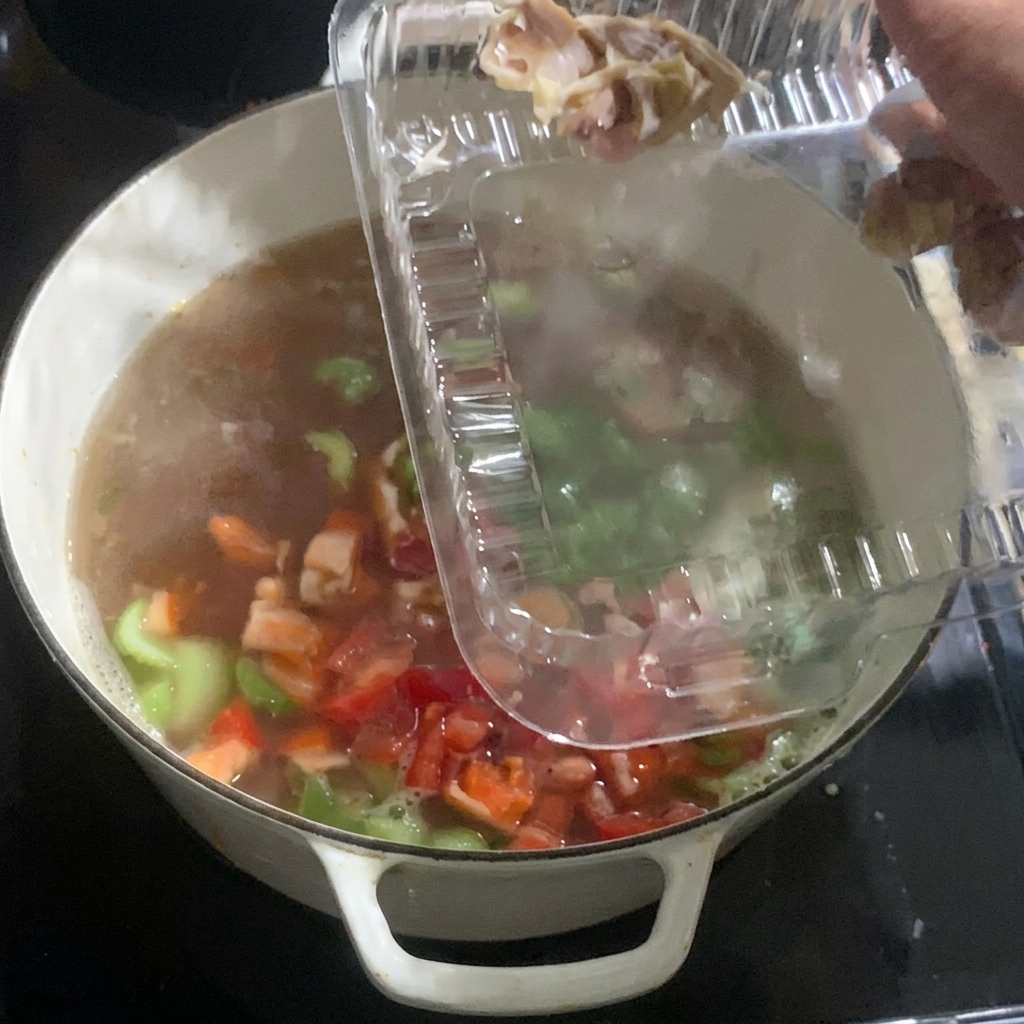 Pieces of cooked chicken being added from a plastic container into a pot of simmering vegetables and broth.