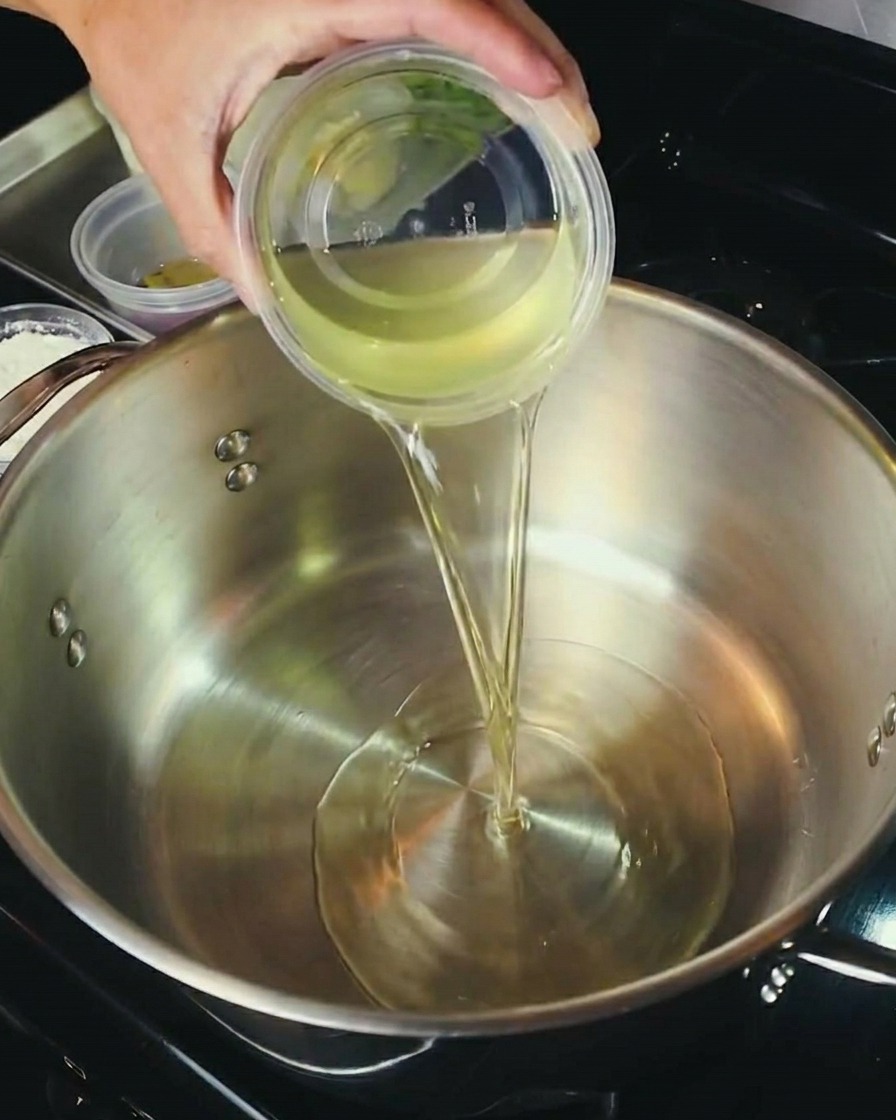 Pouring a mixture of oil and flour into a stainless steel pot to begin cooking the roux.