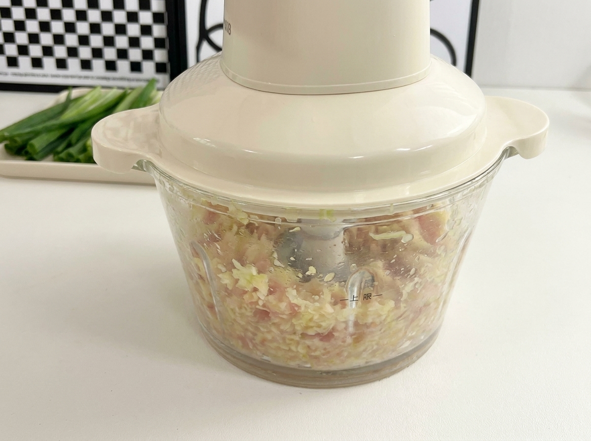 A small food processor actively blending raw chicken and okra seeds into a finely minced texture.
