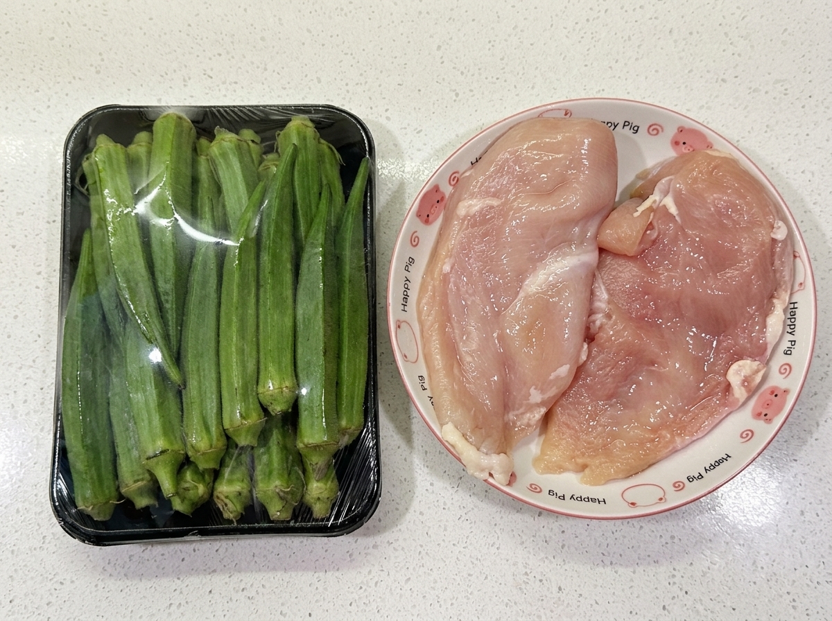 A package of fresh green okra sitting next to two raw chicken breasts on a patterned plate over a white countertop.