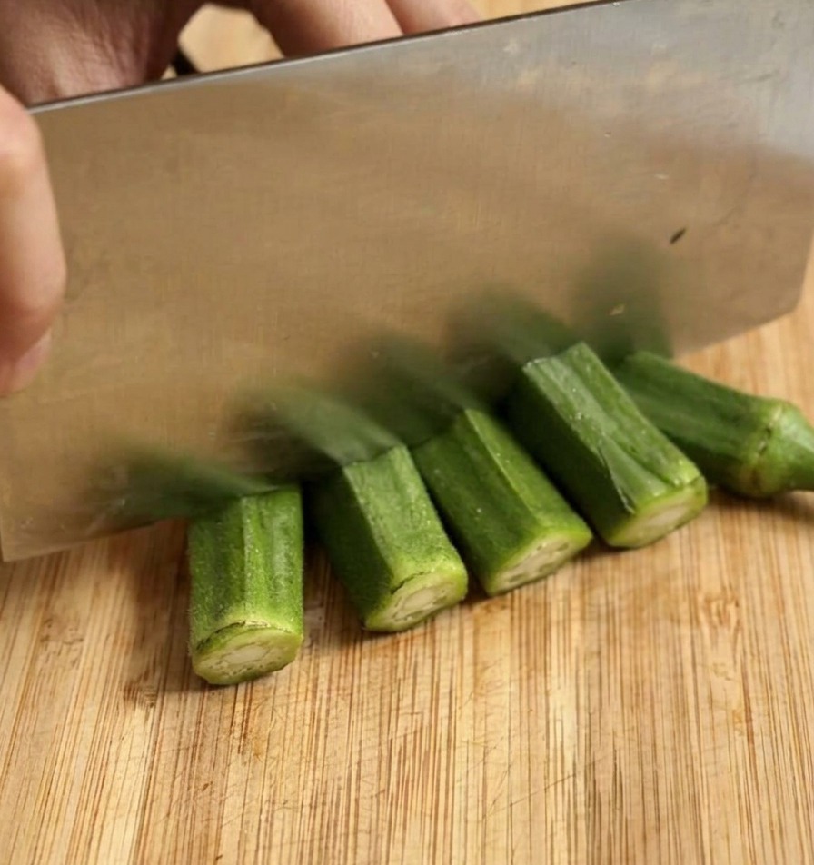 Slicing fresh green okra into thick rounds with a large knife.