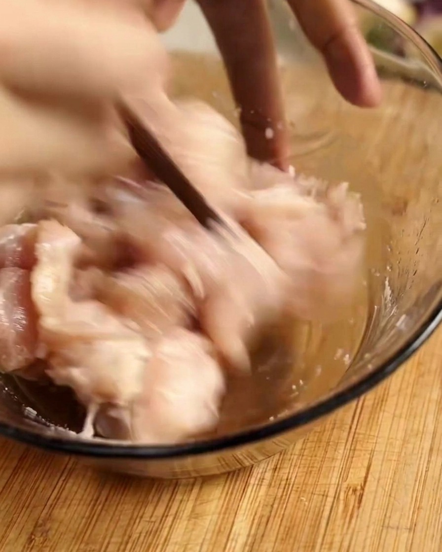 Using chopsticks to rapidly mix raw chicken pieces with marinade in a glass bowl.