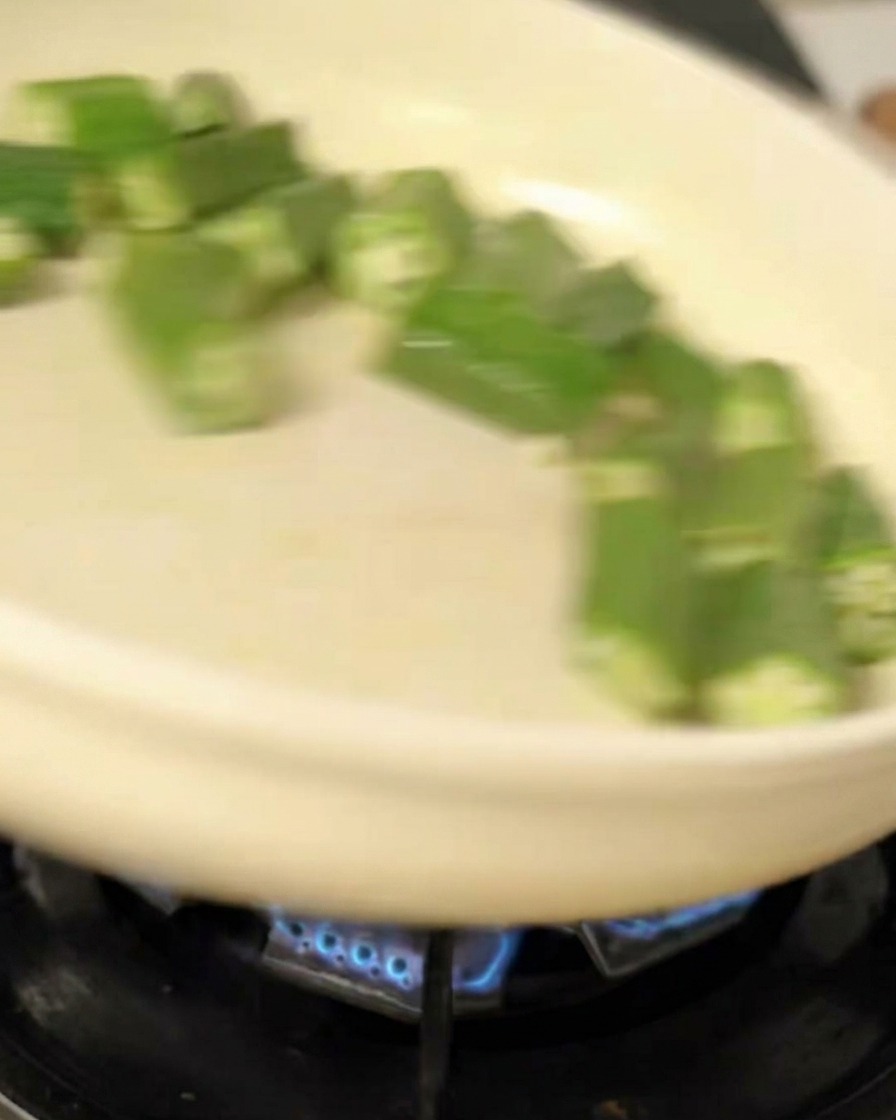 Tossing bright green okra slices in a white skillet over a gas flame.