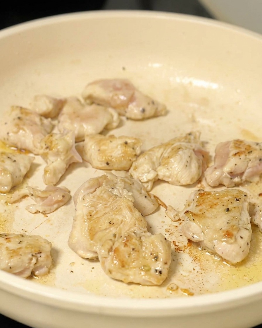 Pieces of diced chicken pan-frying in a skillet until lightly browned.