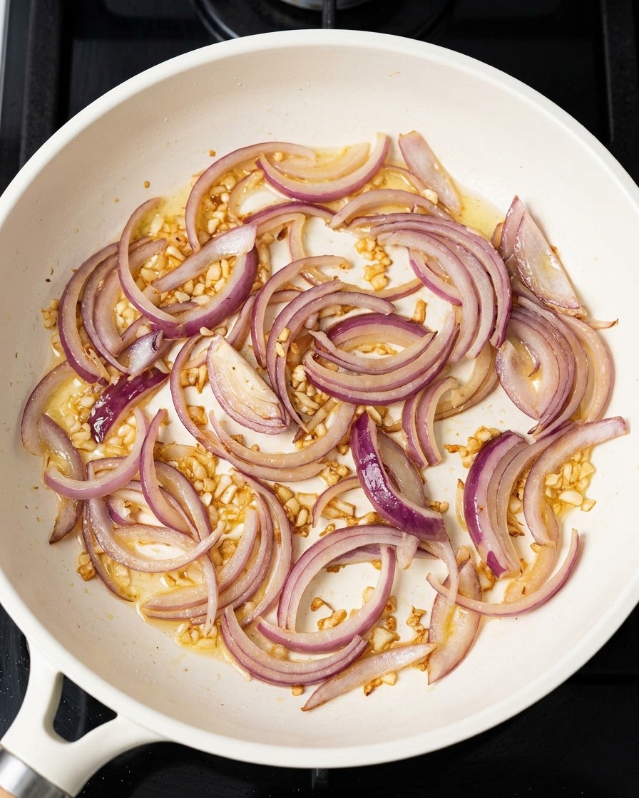 Sliced red onions and chopped garlic sautéing in a pan with residual oil.