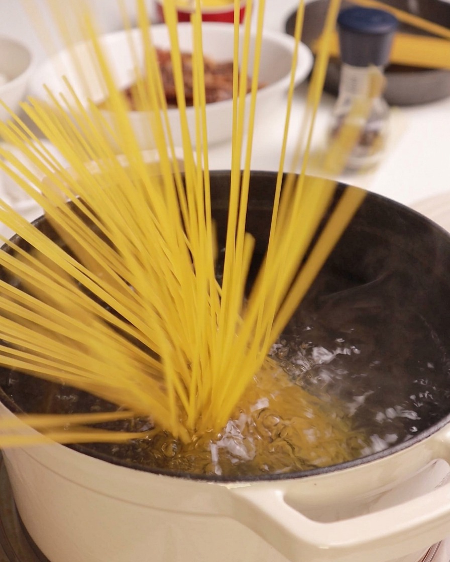 A bunch of dry spaghetti noodles being dropped into a pot of boiling water.