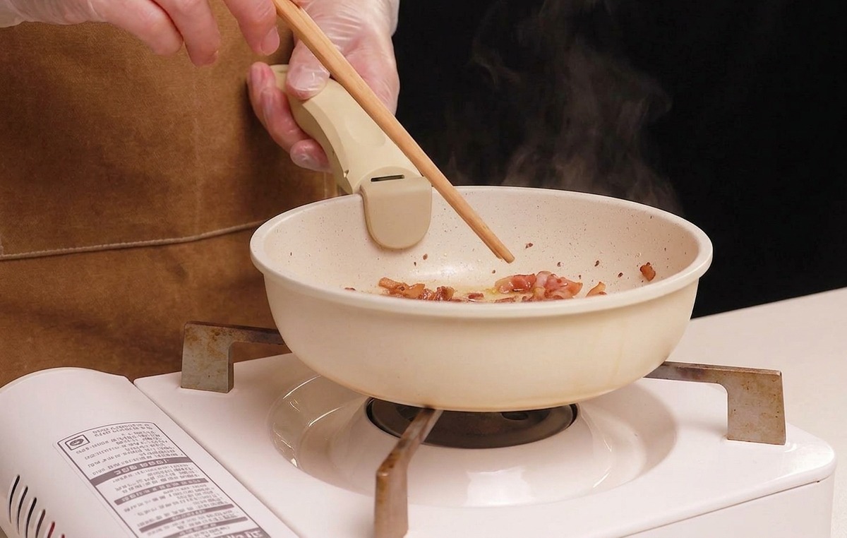 Stirring diced guanciale with chopsticks in a white pan as it browns and renders its fat.