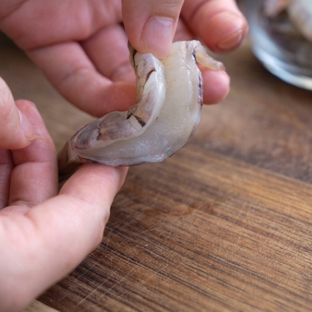 A peeled raw shrimp being held open to reveal the slit down its back for deveining.