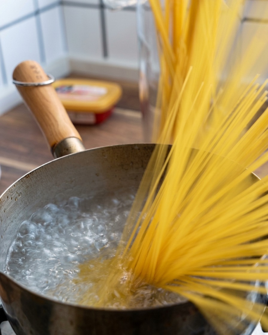 A handful of dry spaghetti noodles being dropped into a pot of vigorously boiling water.