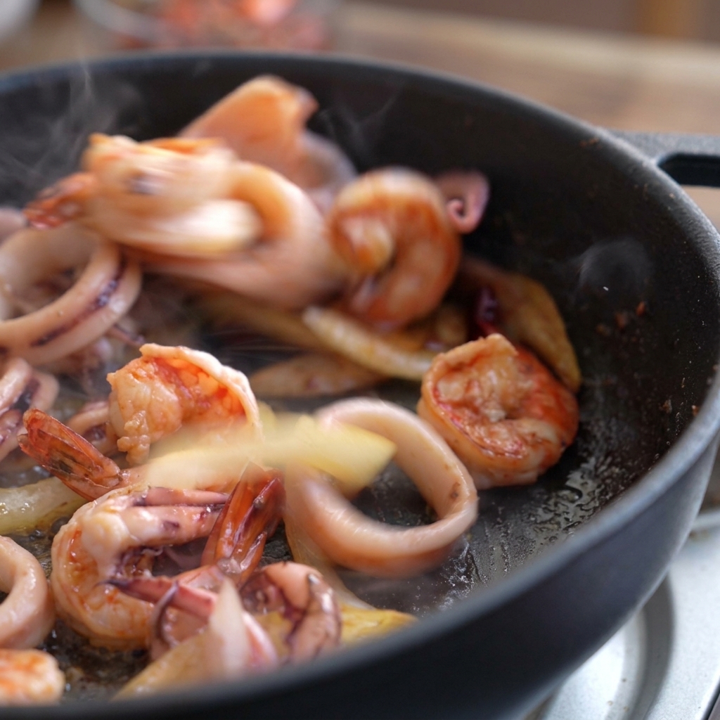 Shrimp and squid rings being tossed rapidly in a hot pan, with the shrimp starting to turn pink.