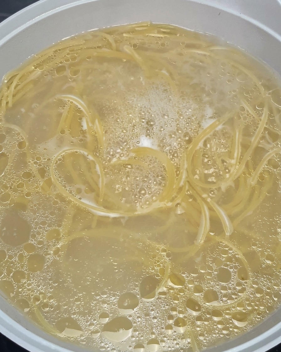 Spaghetti noodles softening and swirling in a pot of vigorously boiling, bubbly hot water.