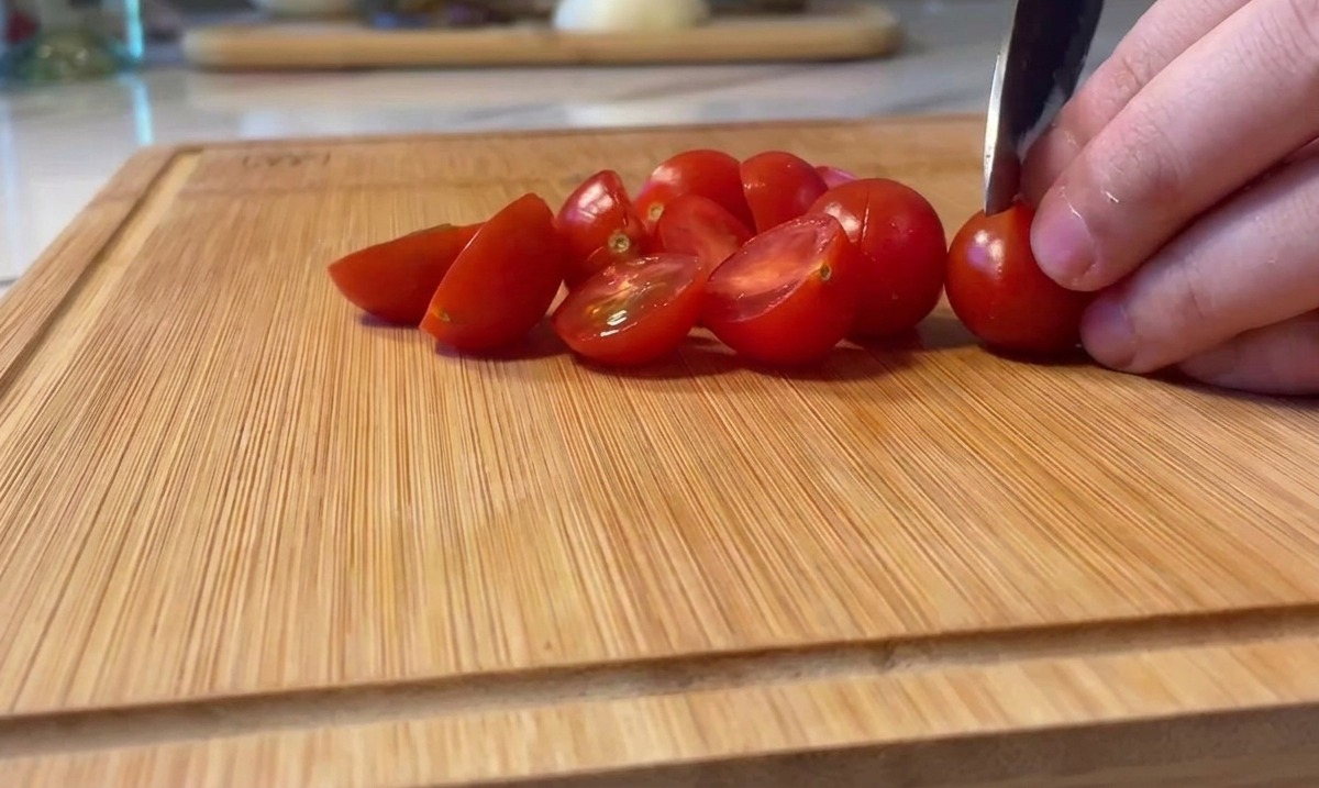 Slicing bright red cherry tomatoes in half on a wooden cutting board.