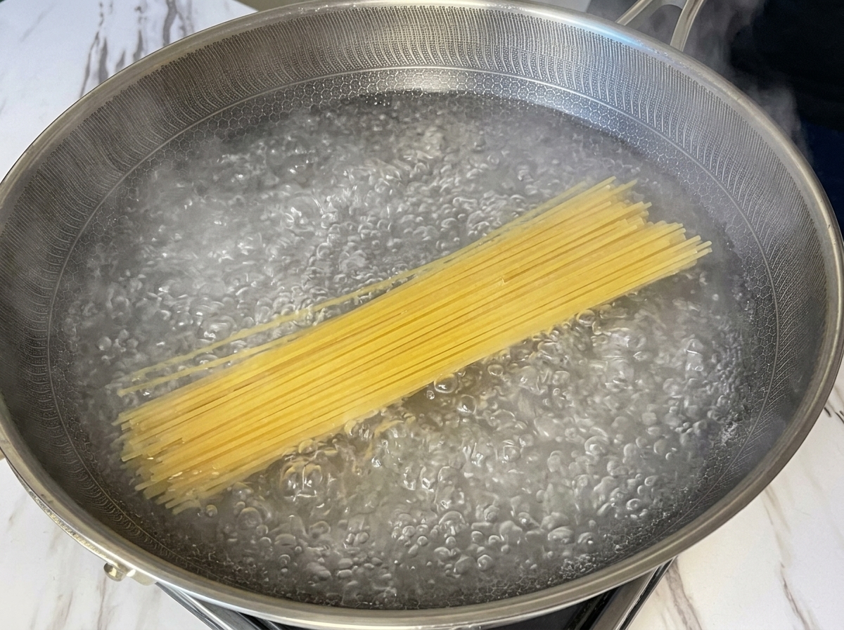 Dry spaghetti noodles submerged in a wide pan of vigorously boiling water.