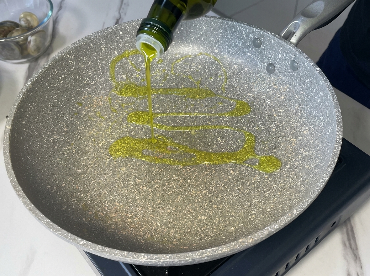 Pouring extra virgin olive oil from a dark green bottle into a grey speckled cooking pan.