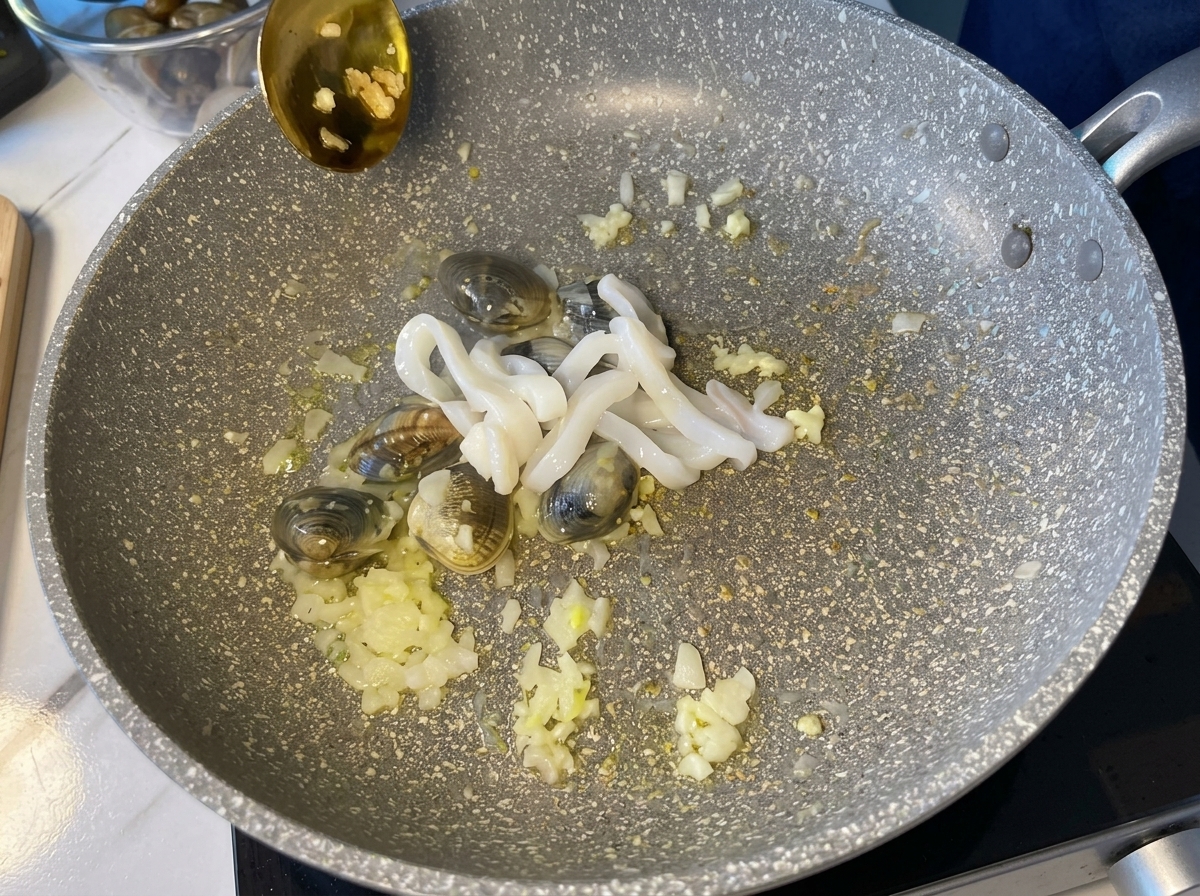 Raw white squid rings being added to a hot pan containing clams and aromatics.