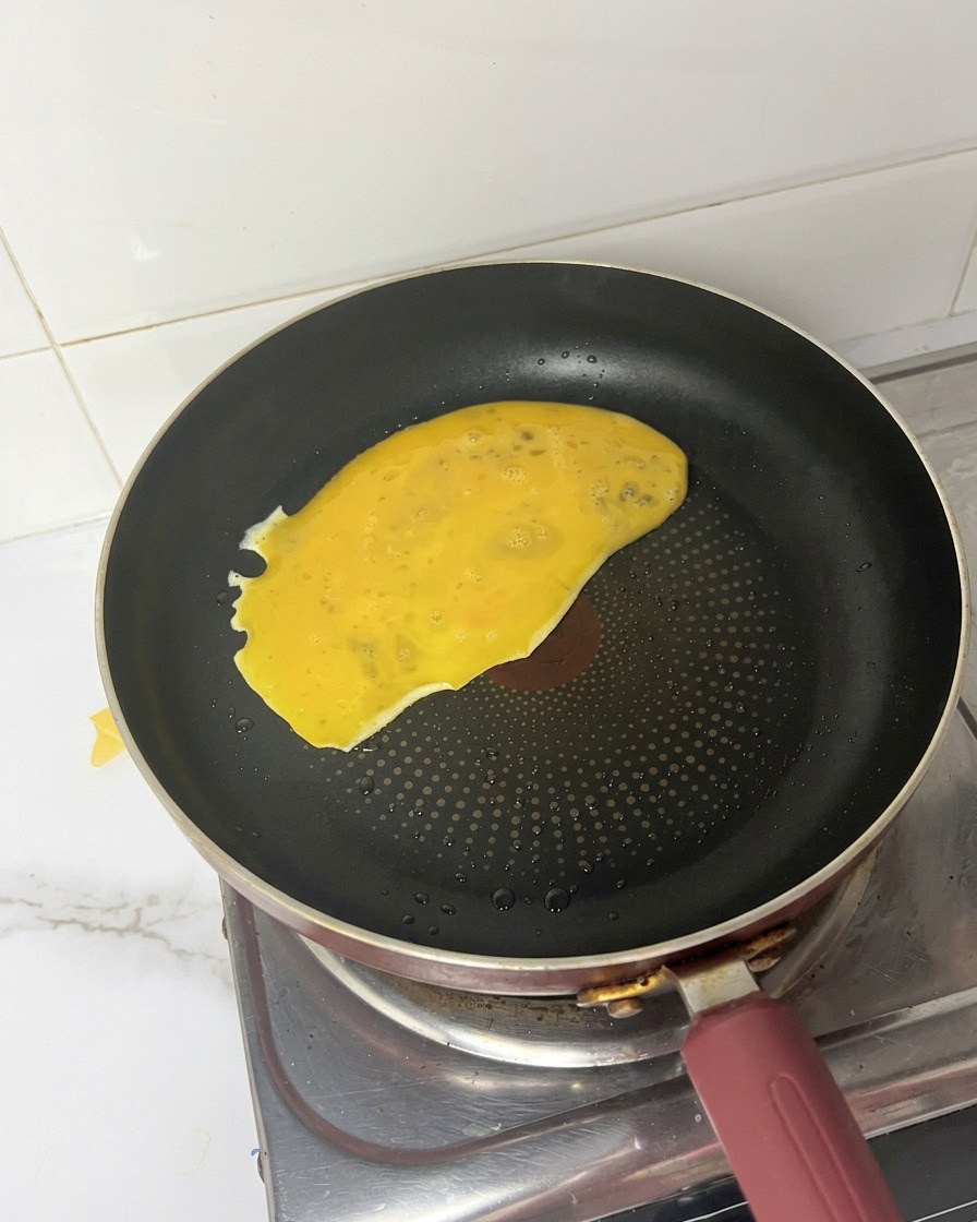 Yellow beaten egg mixture being poured and spreading across a hot black frying pan.