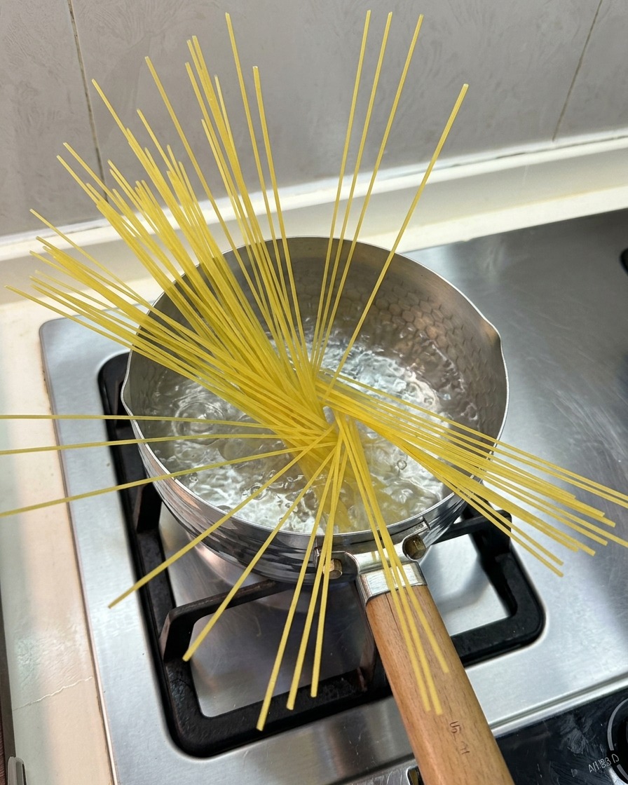 Dry spaghetti noodles fanned out and partially submerged in a small pot of boiling water on a gas stove.