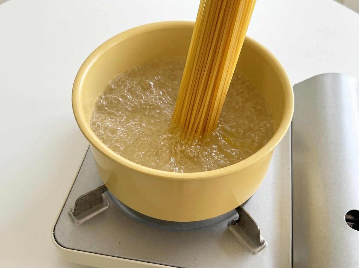 Placing dry spaghetti noodles into a yellow pot filled with boiling water.