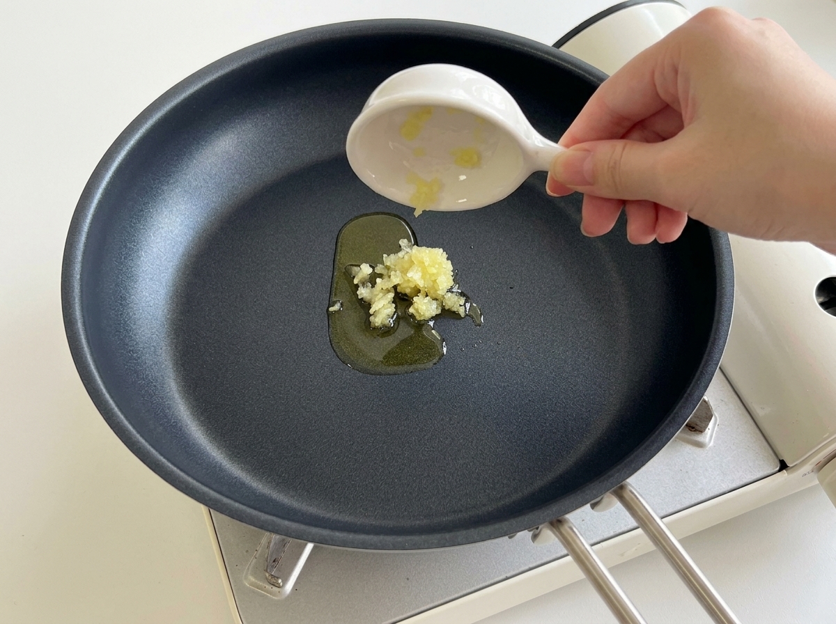 Pouring minced garlic from a small dish into a heated black frying pan with cooking oil.