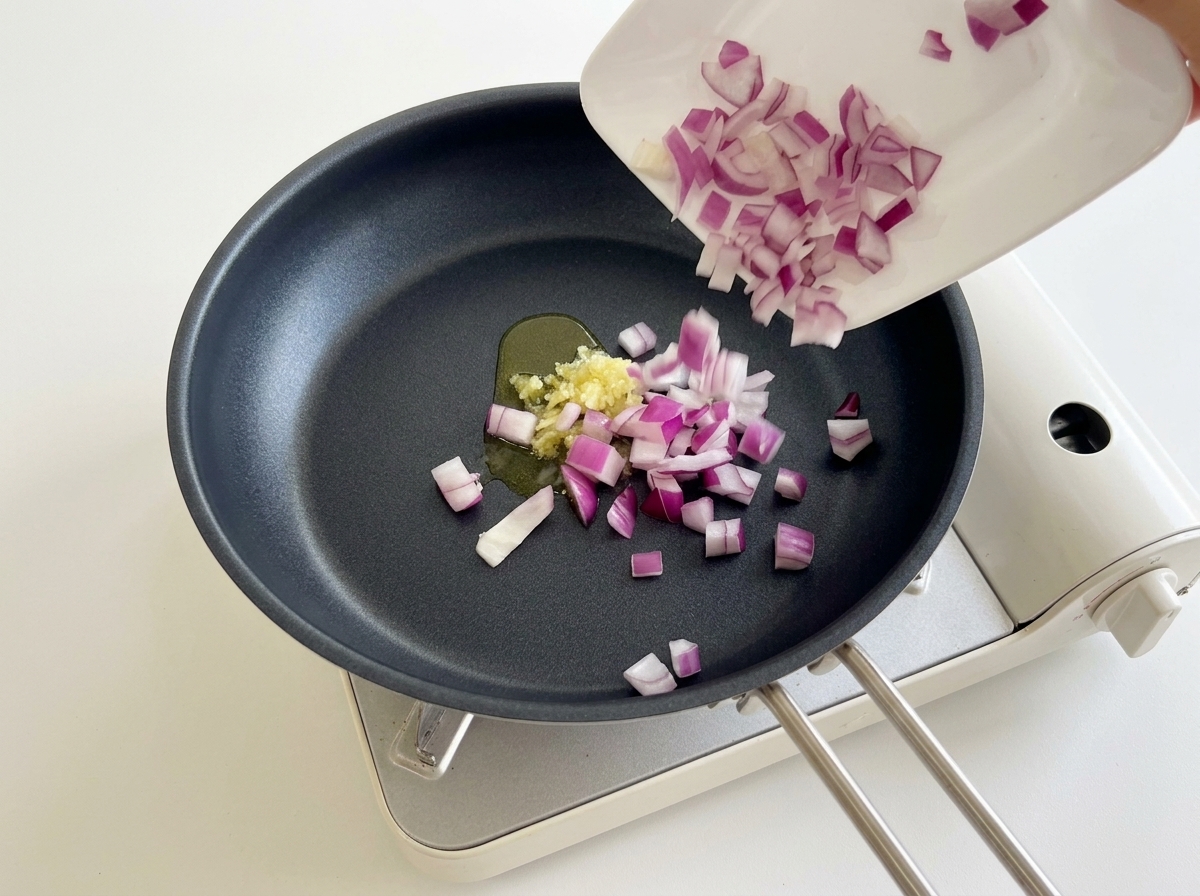 Adding diced red onions to a frying pan with sautéed minced garlic.