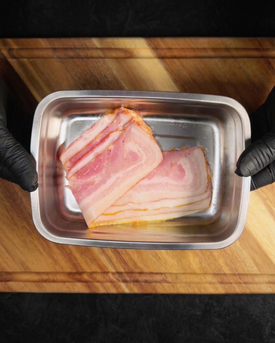 Slices of uncooked bacon placed inside a rectangular metal tray.