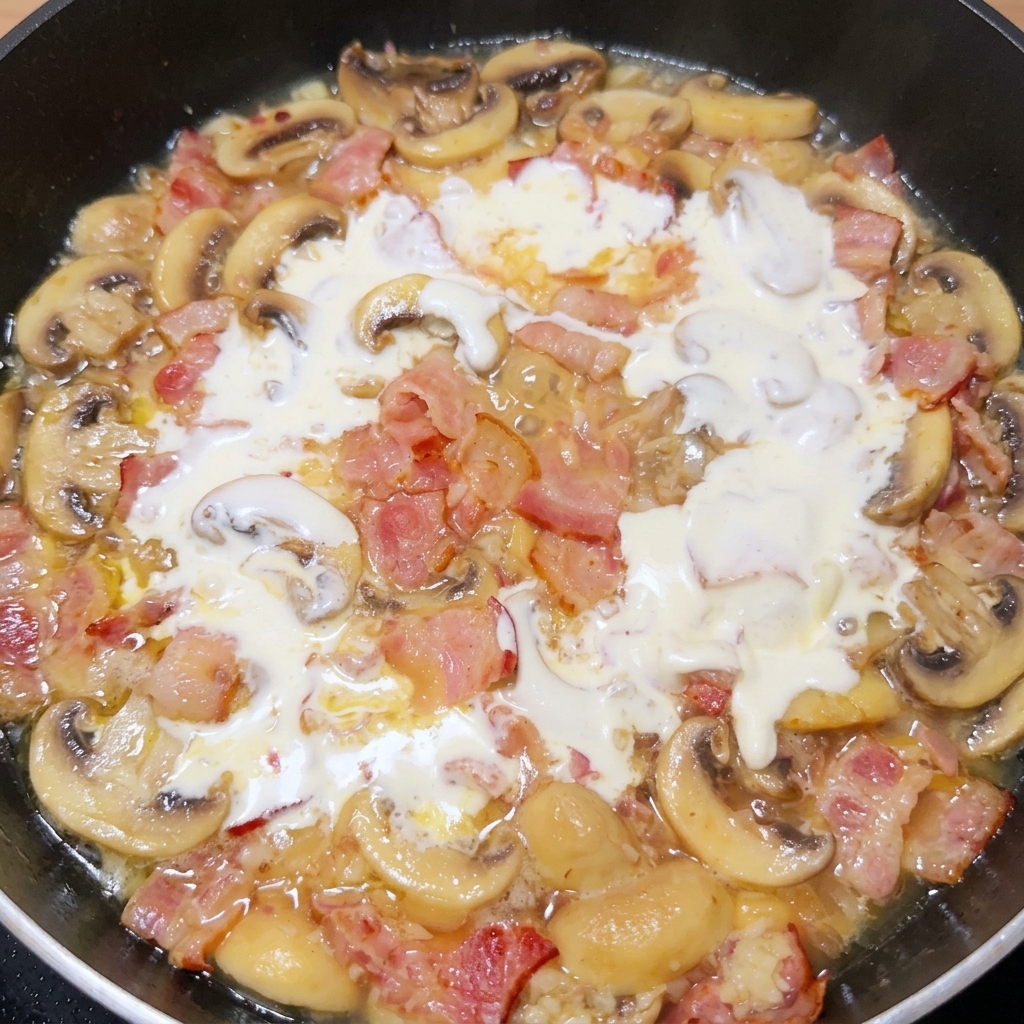 Heavy white cream swirling into a simmering pan of bacon, mushrooms, onions, and garlic.