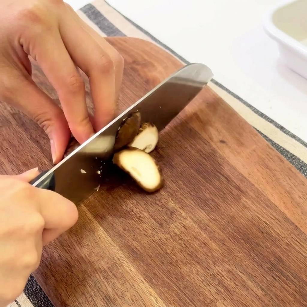 Hands slicing fresh shiitake mushrooms on a wooden cutting board.