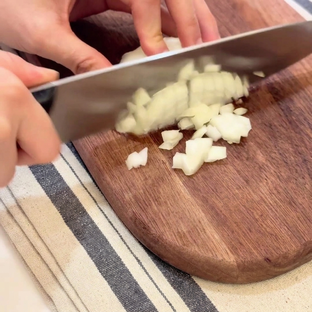 Hands carefully dicing a white onion into small uniform pieces on a wooden cutting board.