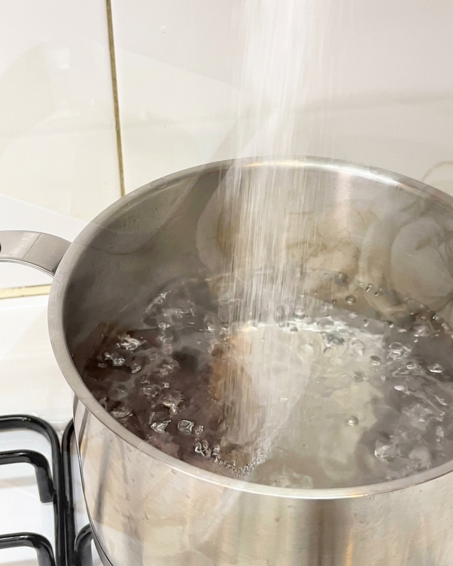 Salt being poured into a stainless steel pot of vigorously boiling water.