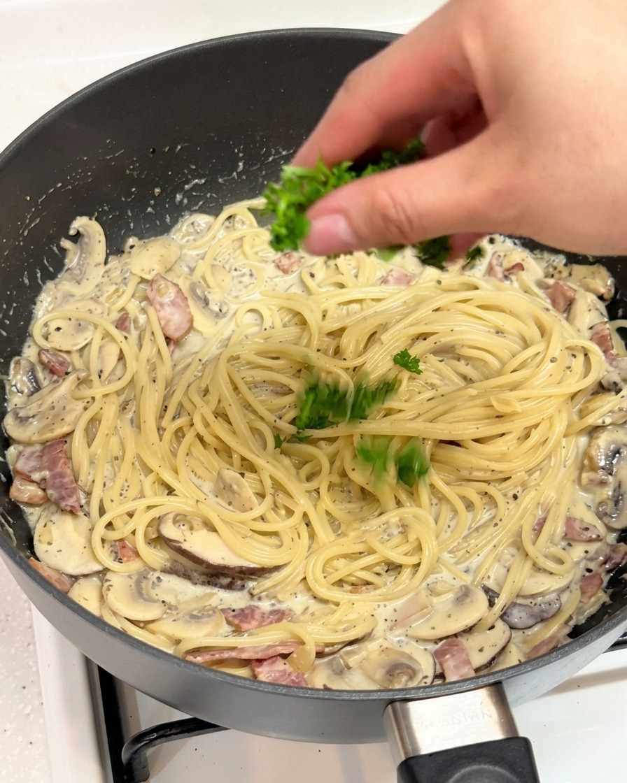 A hand sprinkling freshly chopped bright green parsley over a pan of creamy truffle pasta.