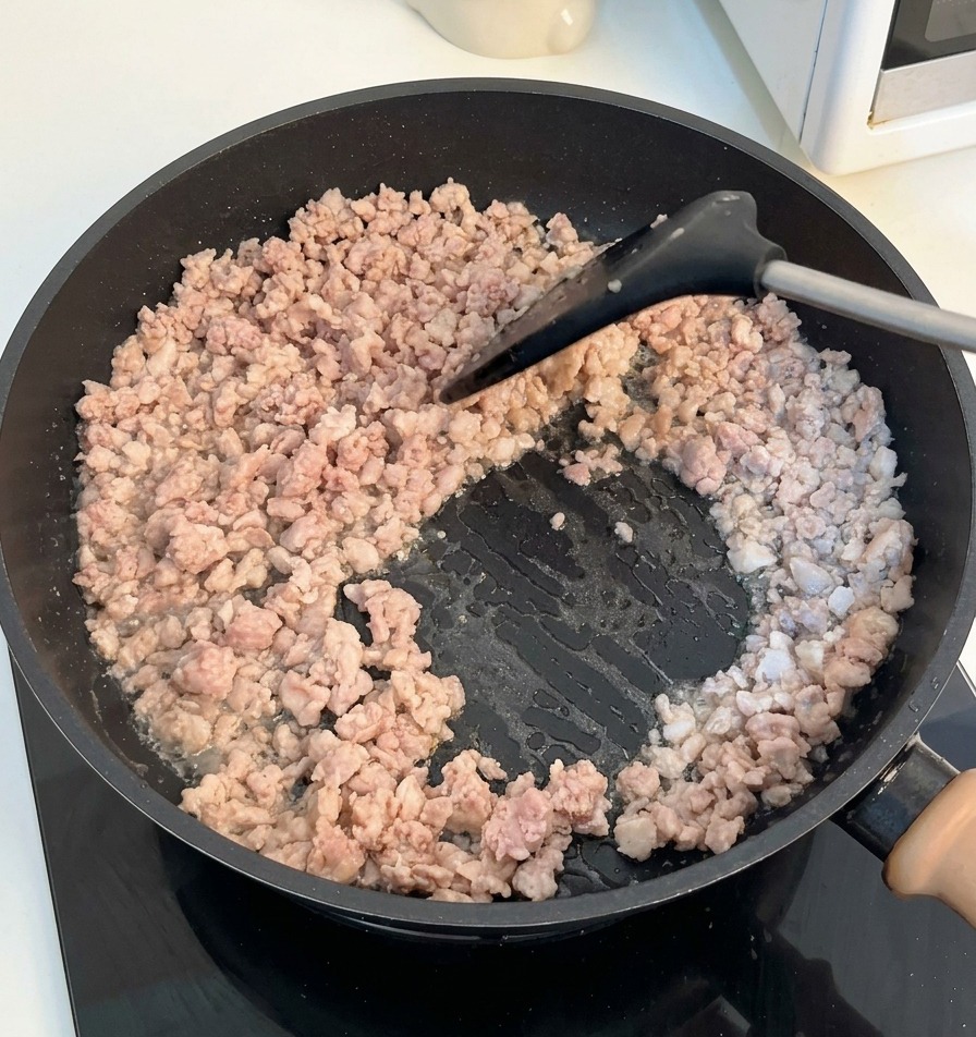 A black spatula stirring and breaking apart browned minced meat in a dark frying pan.