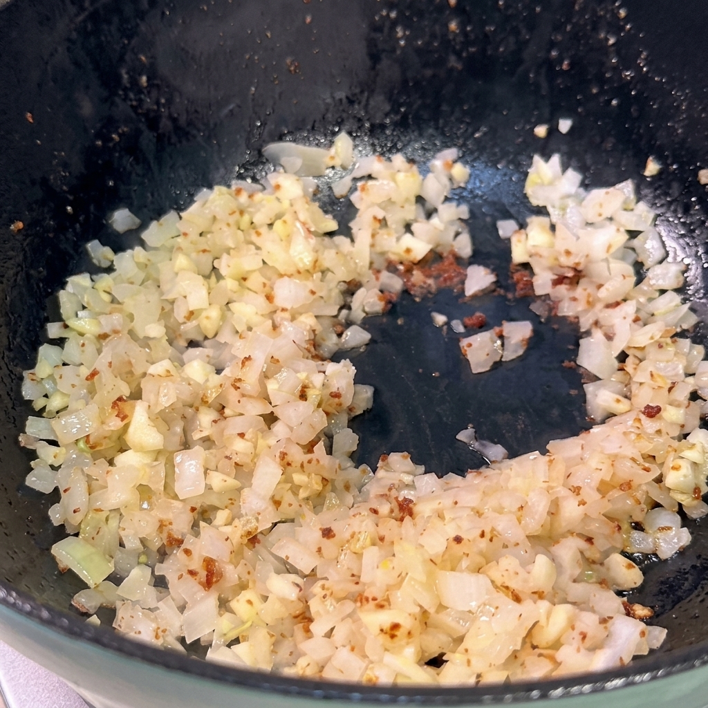 Chopped onions and minced garlic being sautéed in a dark pan, starting to turn translucent.