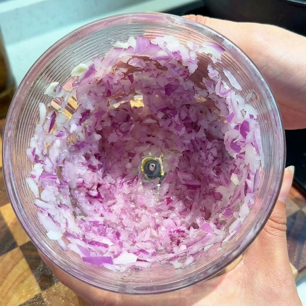 Finely chopped pieces of red onion coating the inside of a clear plastic food processor bowl.